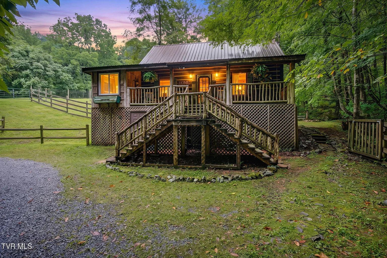 Bear cabin at Misty Hollow glowing at dusk with porch lights, meadow, and timbered hills